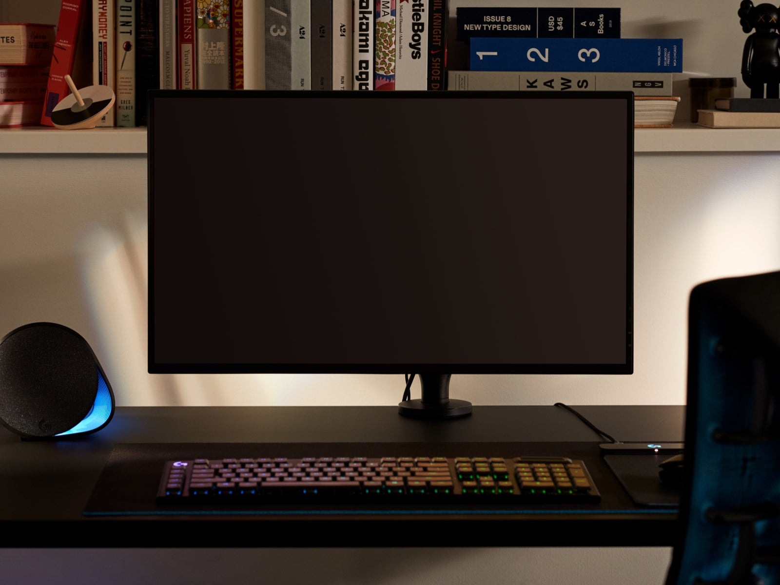 Ein großer Bildschirm, der veranschaulicht, dass der Ollin Monitorarm Bildschirme jeder Größe trägt, ist an dem Arm auf einem Schreibtisch befestigt. Im Vordergrund sieht man eine Tastatur, im Hintergrund Gegenstände auf einem Regal.