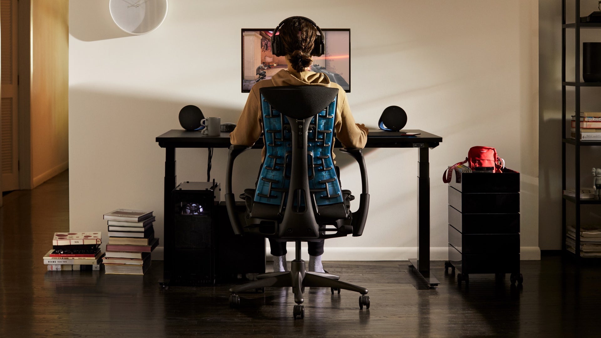 Eine Person in einem Wohnraum sitzt auf dem Embody Gaming-Stuhl und schaut auf einen Bildschirm am Ollin Monitorarm, der auf dem Gaming-Schreibtisch steht.